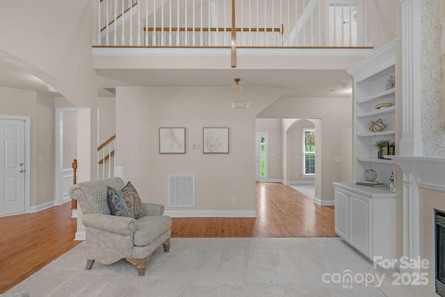 living area featuring a fireplace, a towering ceiling, and light hardwood / wood-style flooring