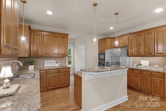 kitchen with black microwave, sink, stainless steel fridge, decorative light fixtures, and a kitchen island