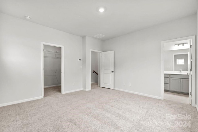 unfurnished bedroom with a spacious closet, ensuite bathroom, sink, a closet, and light colored carpet