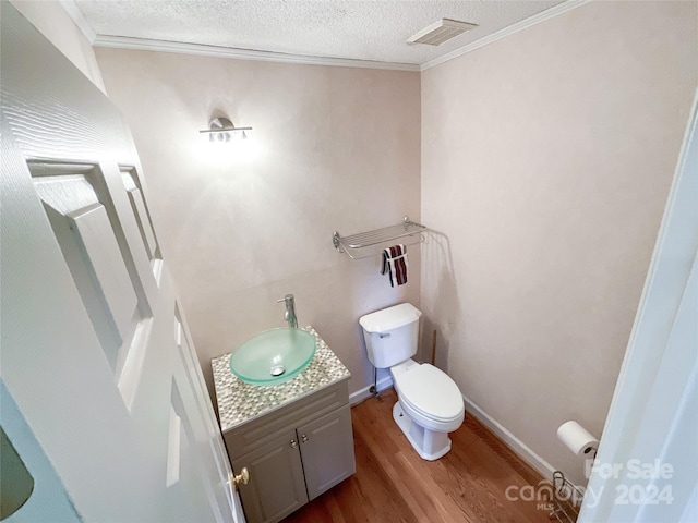 bathroom with a textured ceiling, wood-type flooring, toilet, ornamental molding, and vanity