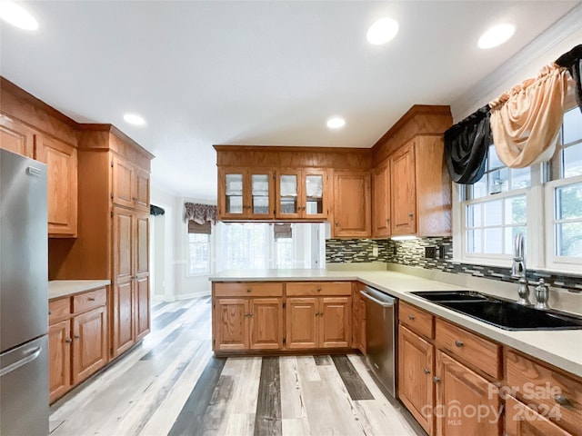 kitchen featuring light hardwood / wood-style flooring, kitchen peninsula, sink, appliances with stainless steel finishes, and tasteful backsplash