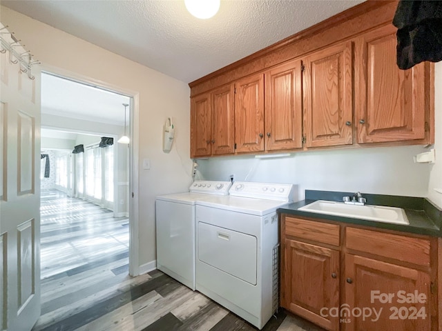 laundry area with sink, a textured ceiling, washer and clothes dryer, cabinets, and light hardwood / wood-style flooring