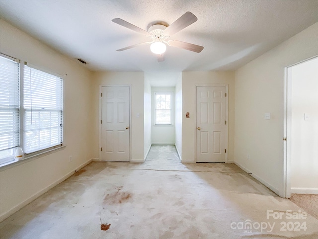 empty room with a textured ceiling, a healthy amount of sunlight, light colored carpet, and ceiling fan