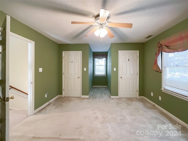 unfurnished bedroom with a textured ceiling, light colored carpet, and ceiling fan