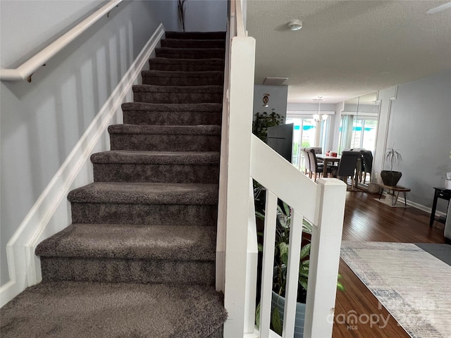 staircase with a notable chandelier, wood-type flooring, and a textured ceiling