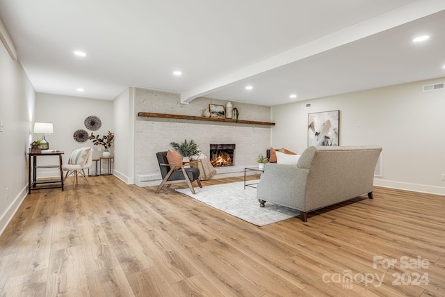 living room featuring beamed ceiling, light wood-type flooring, and a fireplace