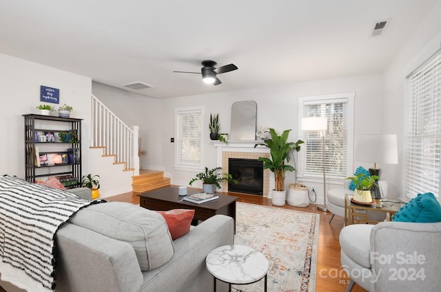 living room featuring a tiled fireplace, wood-type flooring, and ceiling fan