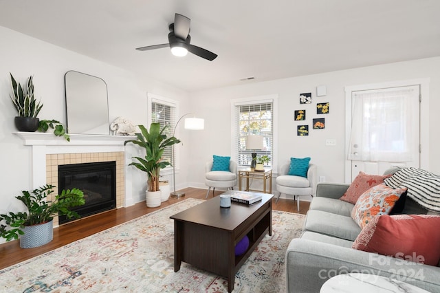 living room featuring hardwood / wood-style floors, a tiled fireplace, and ceiling fan