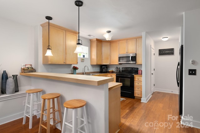 kitchen featuring light brown cabinets, kitchen peninsula, black range with electric stovetop, hanging light fixtures, and a kitchen bar