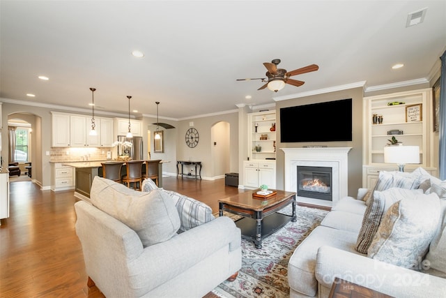 living room featuring ceiling fan, built in features, dark hardwood / wood-style flooring, and ornamental molding