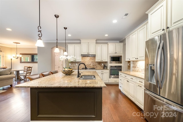 kitchen featuring appliances with stainless steel finishes, decorative light fixtures, dark hardwood / wood-style floors, light stone countertops, and an island with sink