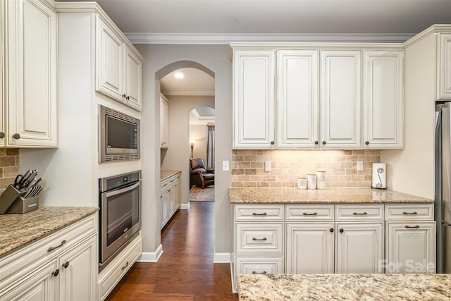 kitchen featuring dark wood-type flooring, light stone counters, appliances with stainless steel finishes, and backsplash