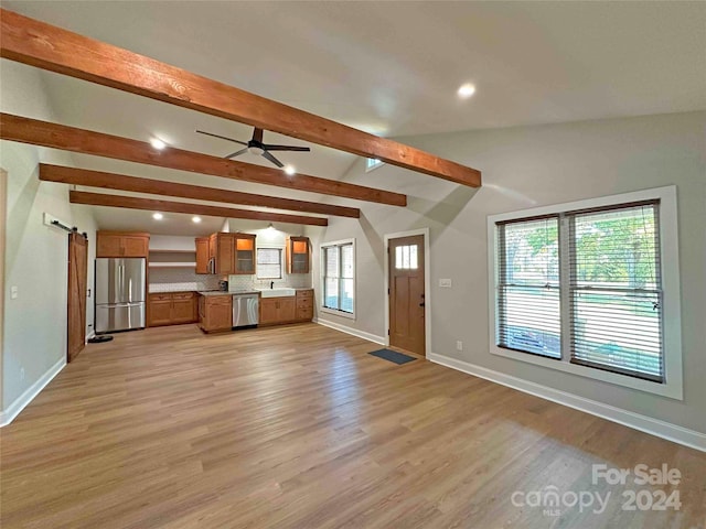 unfurnished living room featuring vaulted ceiling with beams, light hardwood / wood-style flooring, plenty of natural light, and a barn door