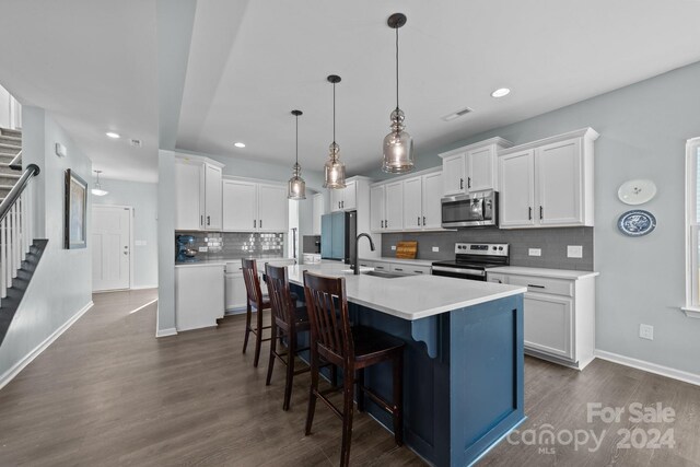 kitchen with an island with sink, hanging light fixtures, stainless steel appliances, sink, and white cabinets