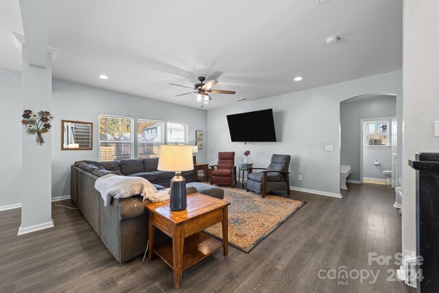 living room with dark wood-type flooring, ceiling fan, and a wealth of natural light