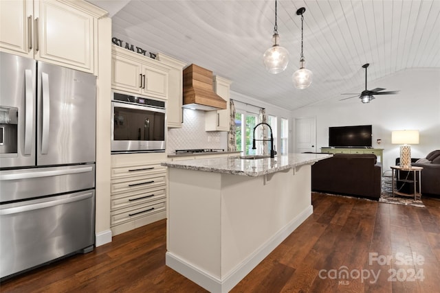 kitchen with lofted ceiling, light stone countertops, dark wood-type flooring, cream cabinetry, and stainless steel appliances