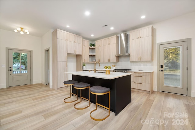 kitchen featuring a wealth of natural light, light brown cabinets, a kitchen island with sink, and wall chimney exhaust hood