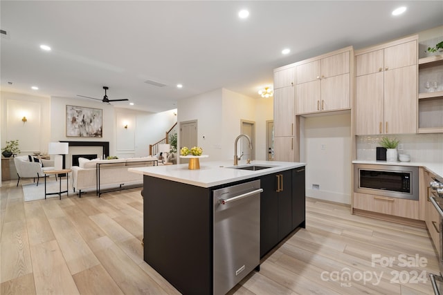 kitchen featuring sink, light brown cabinets, light hardwood / wood-style floors, a center island with sink, and appliances with stainless steel finishes