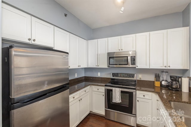 kitchen with dark hardwood / wood-style flooring, appliances with stainless steel finishes, white cabinetry, and dark stone counters