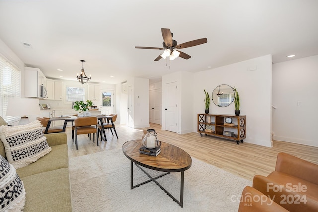 living room with ceiling fan with notable chandelier and light hardwood / wood-style floors