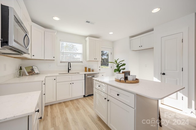 kitchen with stainless steel appliances, sink, a kitchen island, white cabinetry, and light wood-type flooring