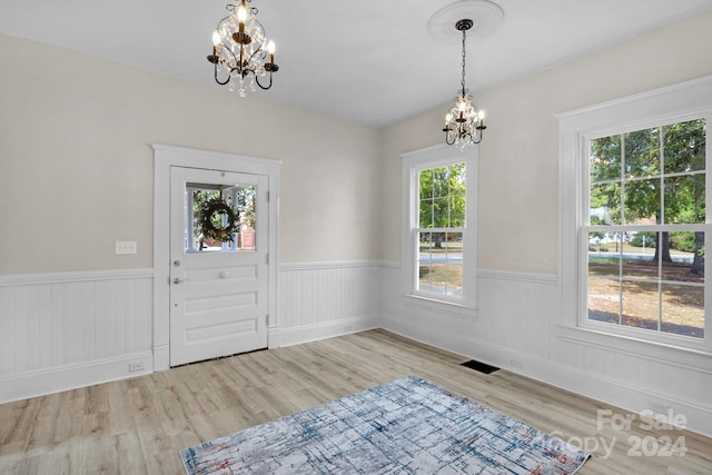 foyer entrance with a notable chandelier, light wood-type flooring, and plenty of natural light