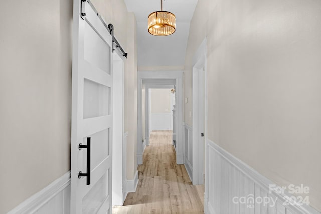 hallway featuring a chandelier, a barn door, and light wood-type flooring