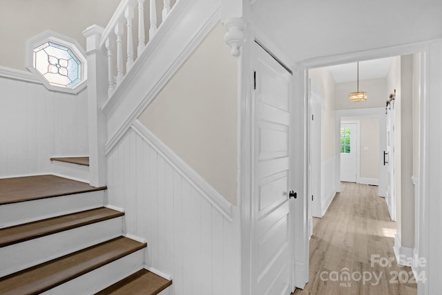 stairs with a notable chandelier, hardwood / wood-style floors, and wooden walls