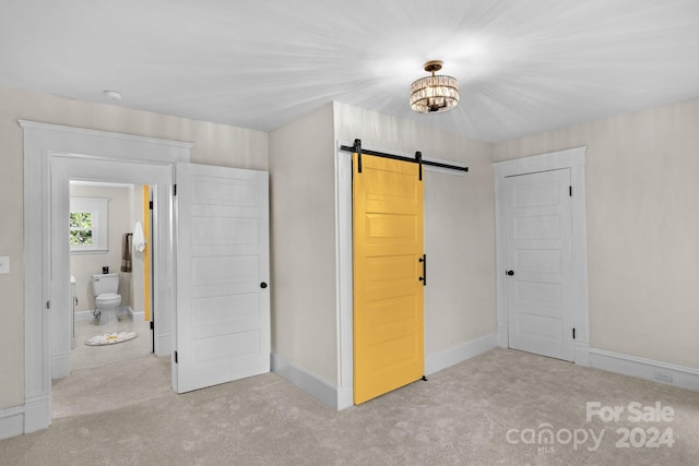 unfurnished bedroom with connected bathroom, a barn door, and light carpet