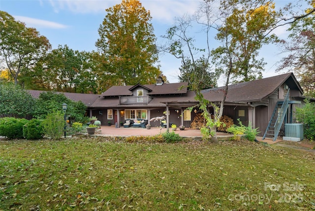 back of property with a balcony, central AC unit, a patio area, and a lawn