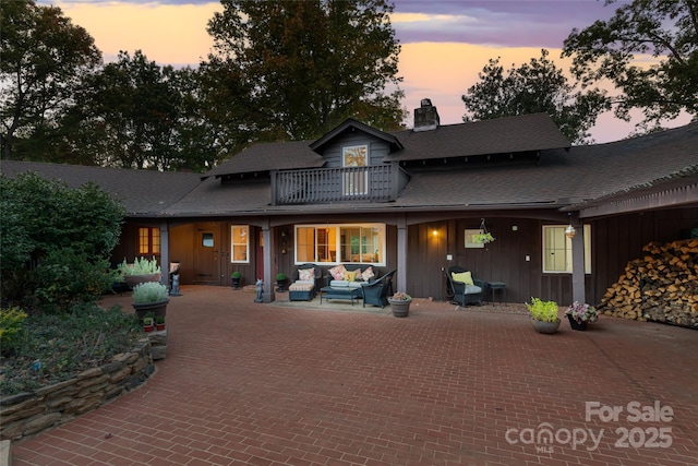 back house at dusk with a balcony and an outdoor hangout area