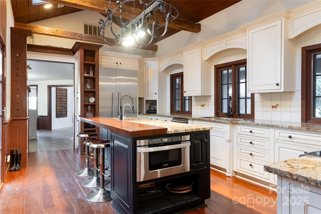 kitchen with stainless steel appliances, dark hardwood / wood-style floors, light stone counters, an island with sink, and decorative backsplash