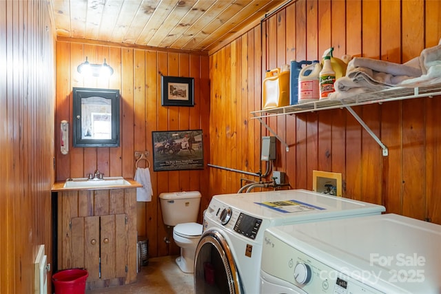 clothes washing area with wood ceiling, independent washer and dryer, wooden walls, and sink