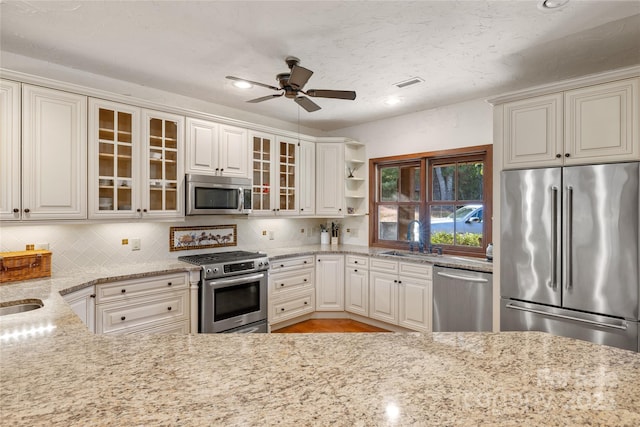 kitchen featuring sink, light stone counters, appliances with stainless steel finishes, ceiling fan, and backsplash