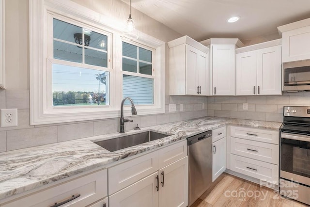 kitchen featuring tasteful backsplash, white cabinets, decorative light fixtures, stainless steel appliances, and a sink