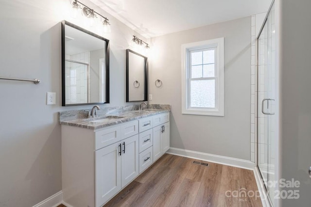 bathroom featuring baseboards, visible vents, wood finished floors, a shower stall, and a sink