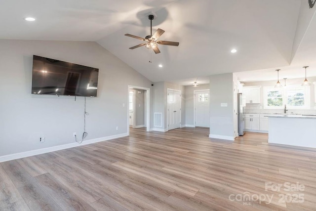 unfurnished living room with a ceiling fan, a sink, vaulted ceiling, light wood-type flooring, and baseboards