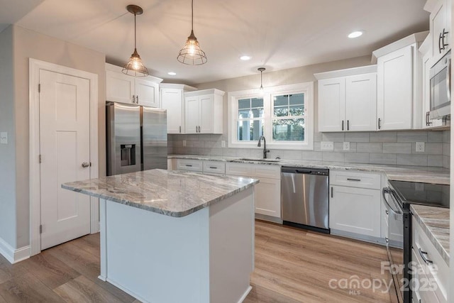 kitchen with appliances with stainless steel finishes, a sink, decorative light fixtures, and white cabinets