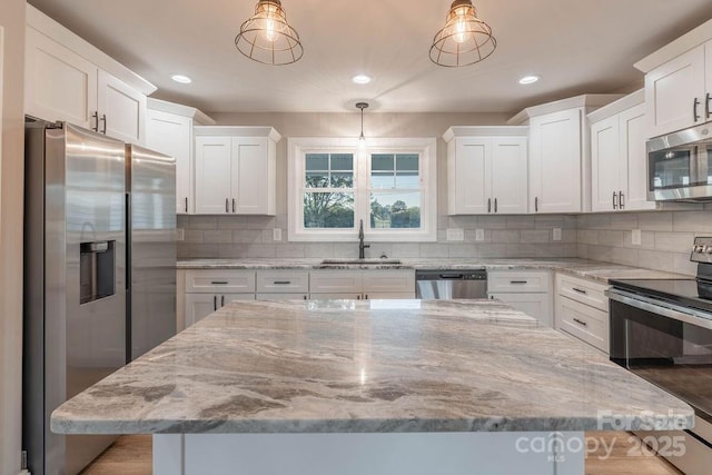 kitchen with pendant lighting, appliances with stainless steel finishes, white cabinetry, a sink, and a kitchen island