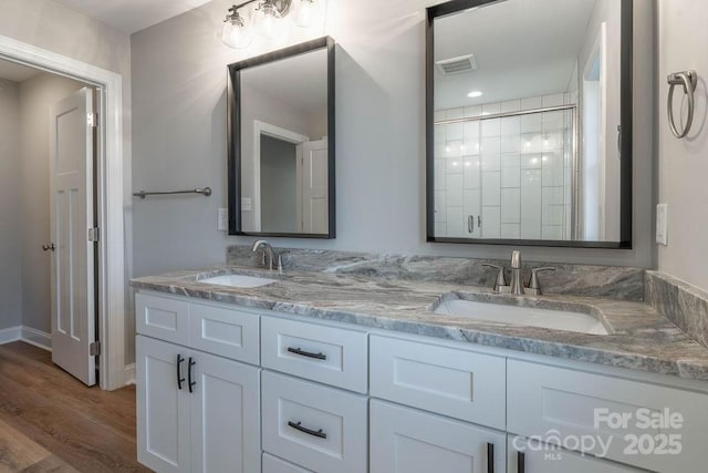 bathroom featuring wood finished floors, visible vents, a sink, and double vanity