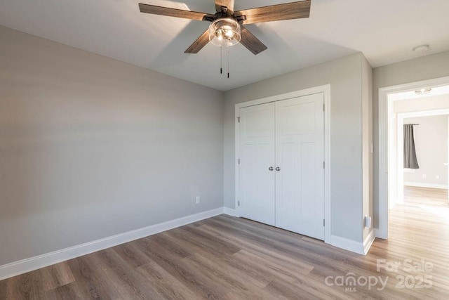 unfurnished bedroom featuring a ceiling fan, a closet, light wood-style flooring, and baseboards