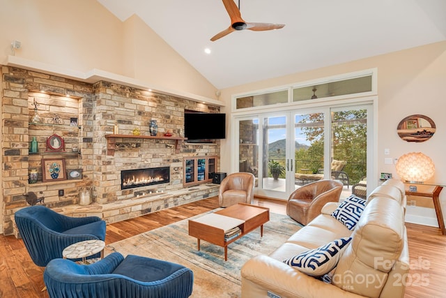 living area with high vaulted ceiling, light wood finished floors, a fireplace, and french doors