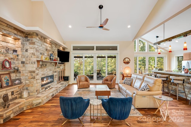 living area with ceiling fan, a fireplace, high vaulted ceiling, and wood finished floors