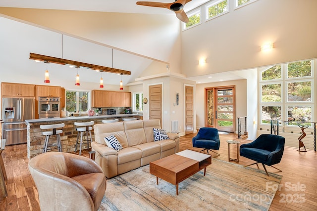 living room featuring ceiling fan, a towering ceiling, and light wood-type flooring