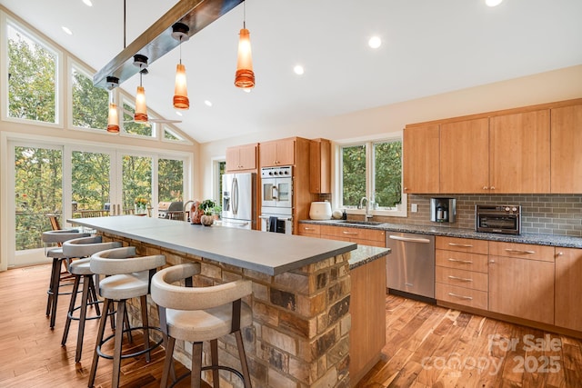 kitchen featuring a kitchen island, appliances with stainless steel finishes, a breakfast bar, pendant lighting, and a sink