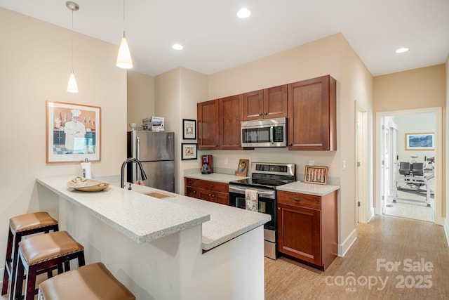 kitchen featuring pendant lighting, sink, appliances with stainless steel finishes, a kitchen bar, and kitchen peninsula