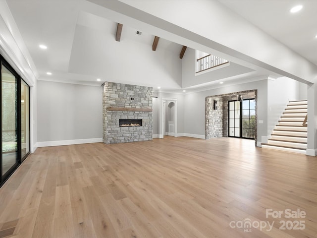 unfurnished living room with beam ceiling, recessed lighting, light wood-style floors, a stone fireplace, and stairs