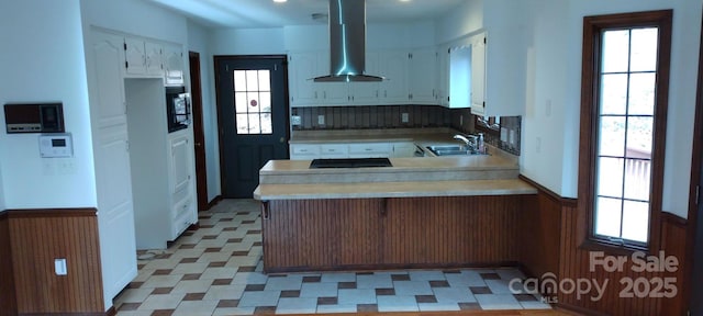 kitchen featuring white cabinets, wall chimney range hood, and kitchen peninsula