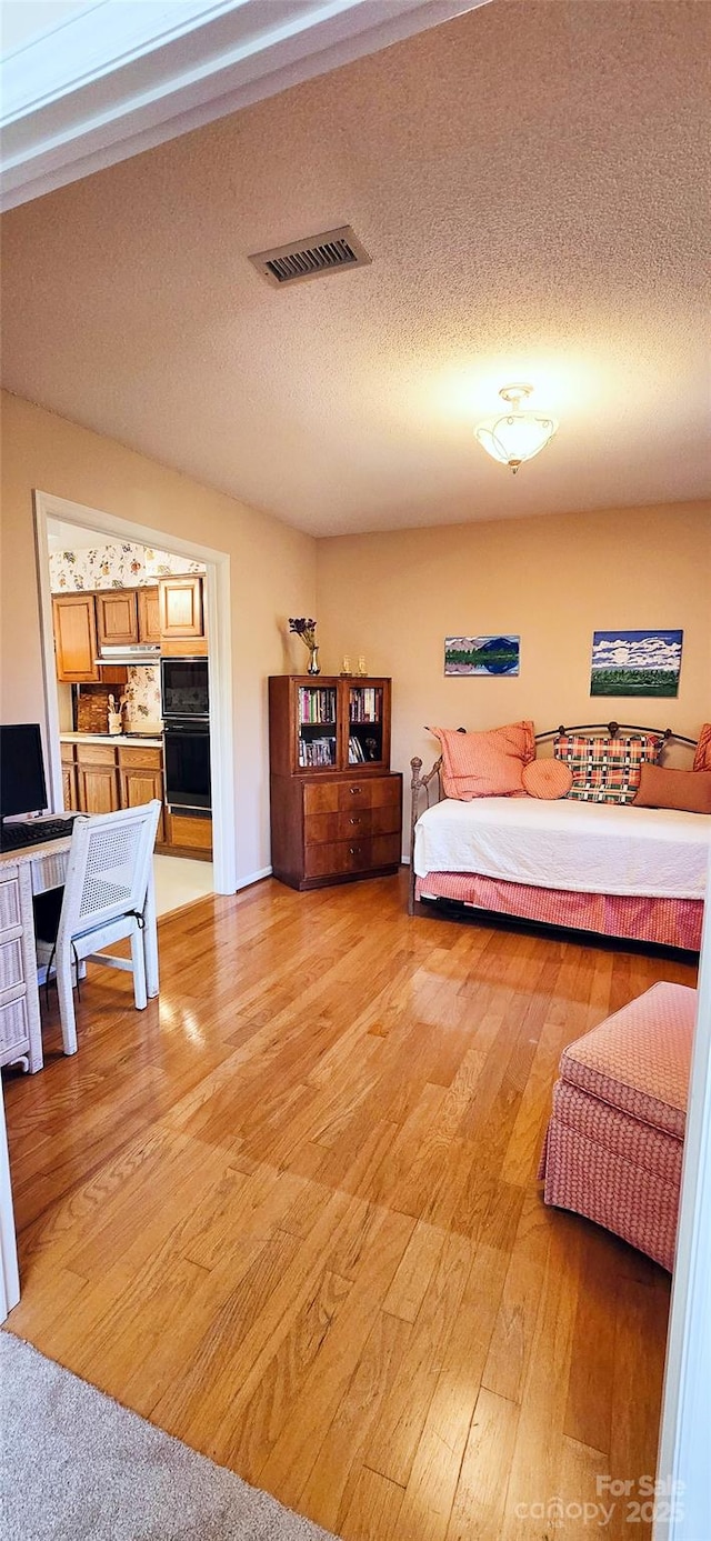 bedroom featuring a textured ceiling, visible vents, and light wood-style floors