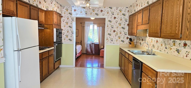 kitchen with under cabinet range hood, a sink, light countertops, black appliances, and wallpapered walls